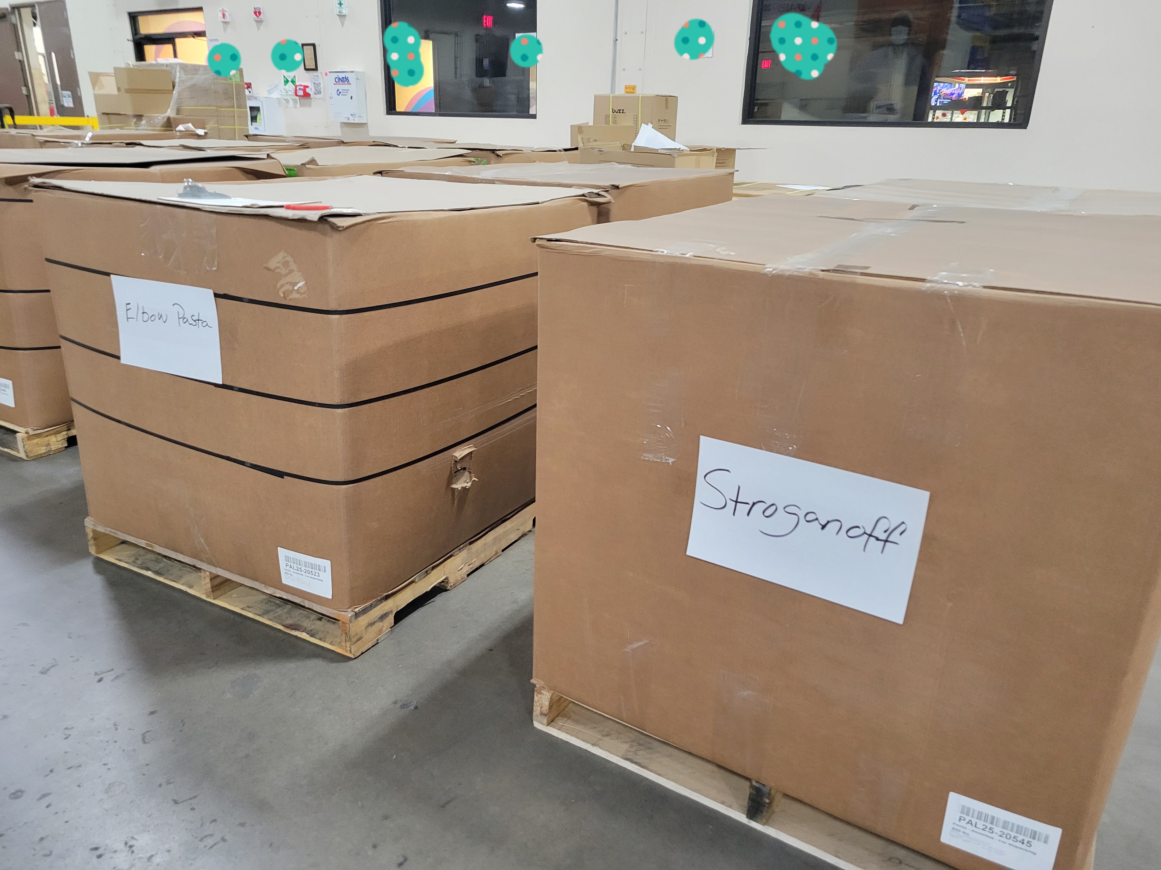 Cardboard containers on pallets with signs listing what kind of pasta is in it.